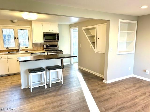 kitchen featuring baseboards, a kitchen bar, appliances with stainless steel finishes, wood finished floors, and a sink