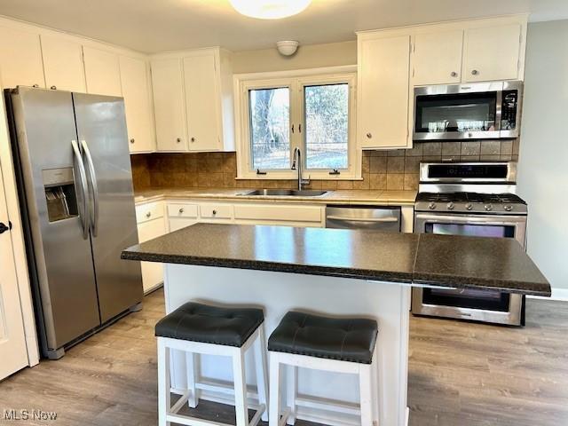 kitchen featuring decorative backsplash, stainless steel appliances, light wood-type flooring, and a sink