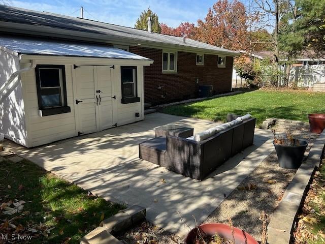 rear view of property featuring a patio, central AC, fence, a yard, and brick siding