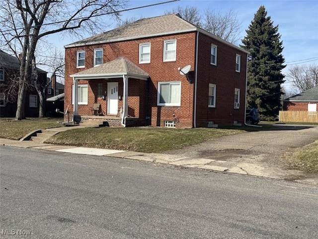 view of front facade with brick siding, roof with shingles, a front lawn, and fence