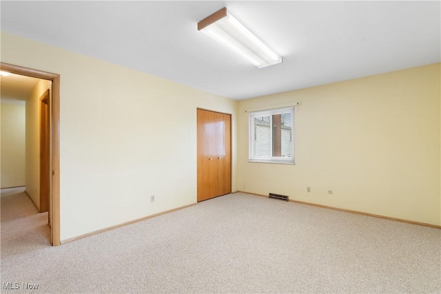 empty room with baseboards, visible vents, and light carpet