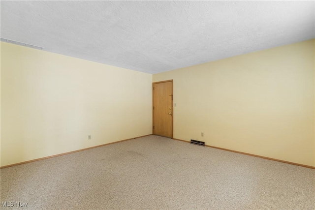 spare room featuring visible vents, baseboards, light colored carpet, and a textured ceiling