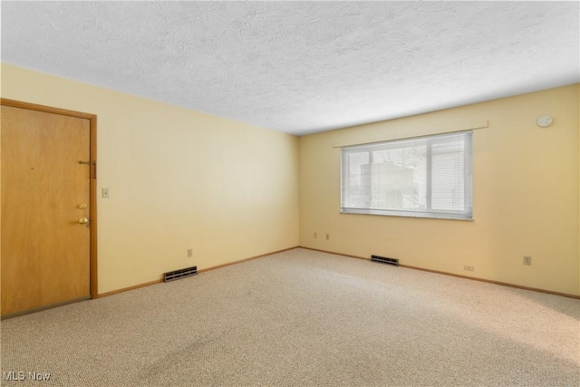 carpeted spare room with visible vents, baseboards, and a textured ceiling