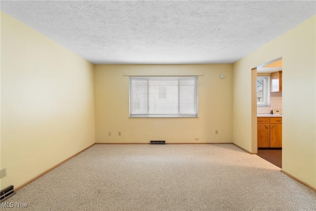 spare room featuring visible vents, light colored carpet, and baseboards