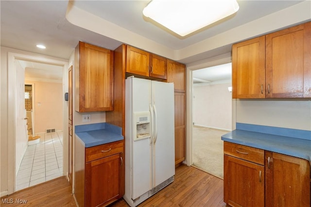 kitchen featuring visible vents, light wood finished floors, white refrigerator with ice dispenser, dark countertops, and brown cabinets