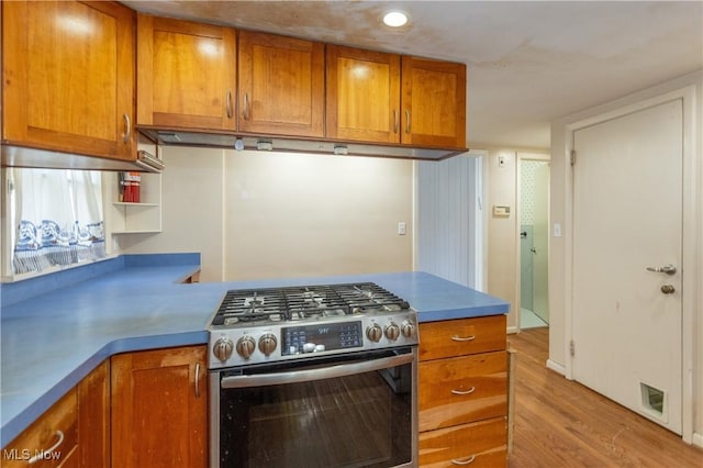 kitchen featuring light wood-type flooring, visible vents, stainless steel range with gas cooktop, a peninsula, and brown cabinetry