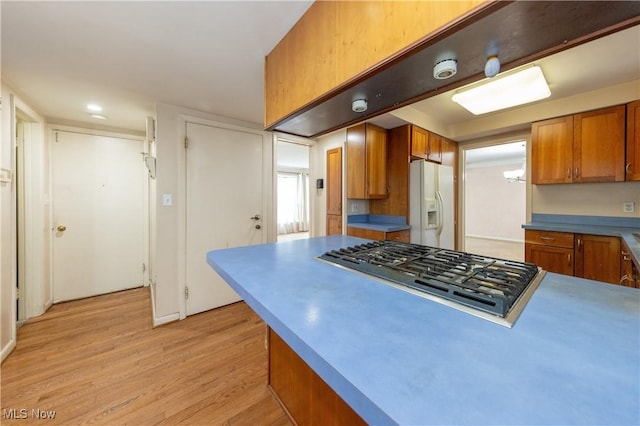 kitchen with stainless steel gas cooktop, light wood-style flooring, light countertops, white refrigerator with ice dispenser, and brown cabinets