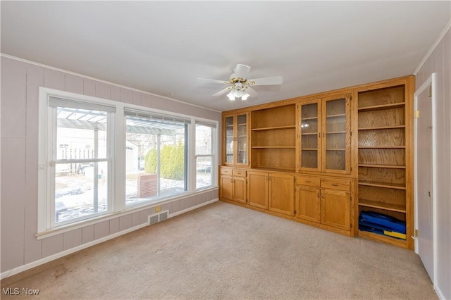 empty room featuring visible vents, light colored carpet, a decorative wall, and ceiling fan