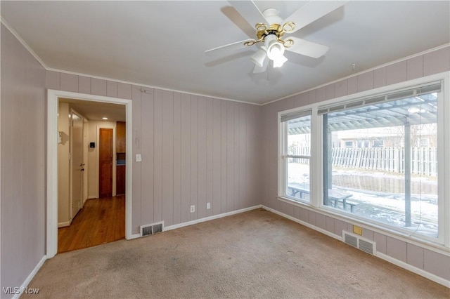 carpeted empty room featuring visible vents, baseboards, ceiling fan, and ornamental molding