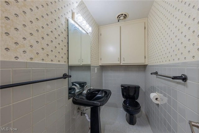 bathroom with a wainscoted wall, toilet, wallpapered walls, and visible vents