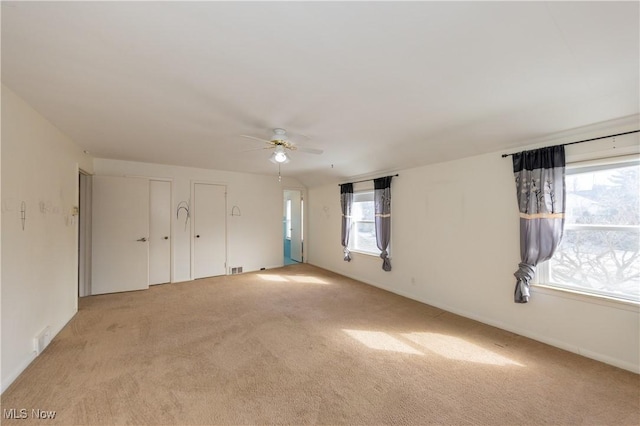 unfurnished bedroom with light carpet, multiple windows, two closets, and ceiling fan