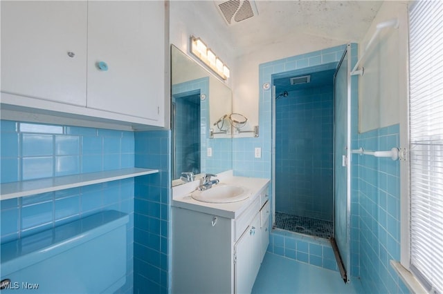 full bath with visible vents, a stall shower, tile walls, and vanity