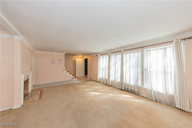 unfurnished living room with stairway, light colored carpet, and a fireplace