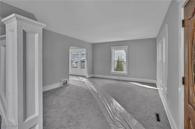 unfurnished living room featuring arched walkways, visible vents, baseboards, and carpet floors