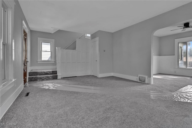 carpeted empty room with arched walkways, visible vents, stairway, and ceiling fan