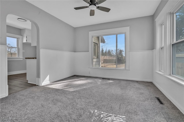 unfurnished room featuring visible vents, arched walkways, a ceiling fan, and carpet flooring