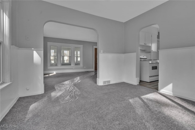 unfurnished living room featuring carpet flooring, visible vents, arched walkways, and baseboards