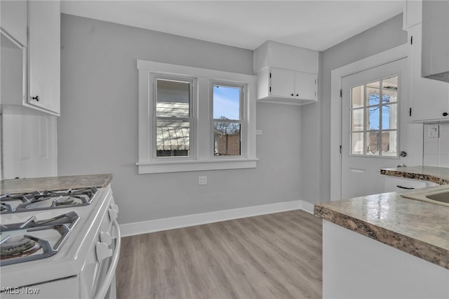 kitchen with white cabinetry, white range with gas cooktop, a healthy amount of sunlight, and baseboards