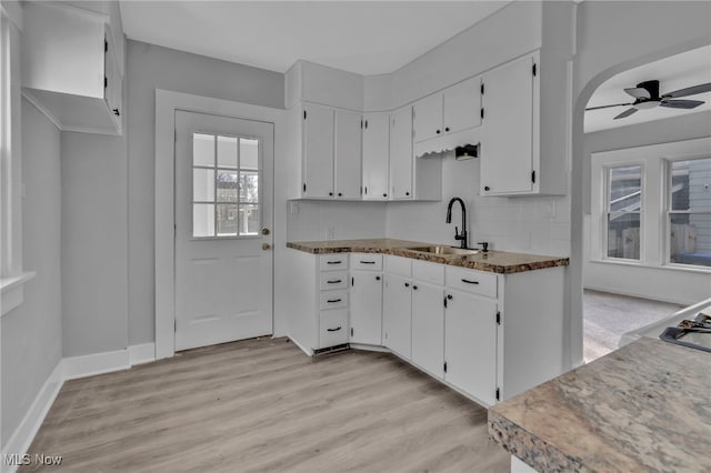 kitchen with light wood-type flooring, a sink, tasteful backsplash, white cabinets, and ceiling fan