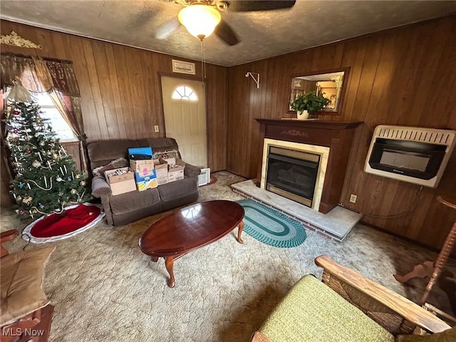 living room with wooden walls, ceiling fan, carpet, heating unit, and a glass covered fireplace