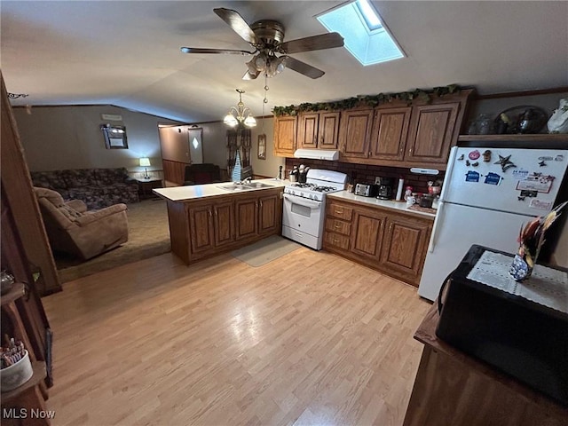 kitchen with lofted ceiling with skylight, under cabinet range hood, a sink, white appliances, and a peninsula