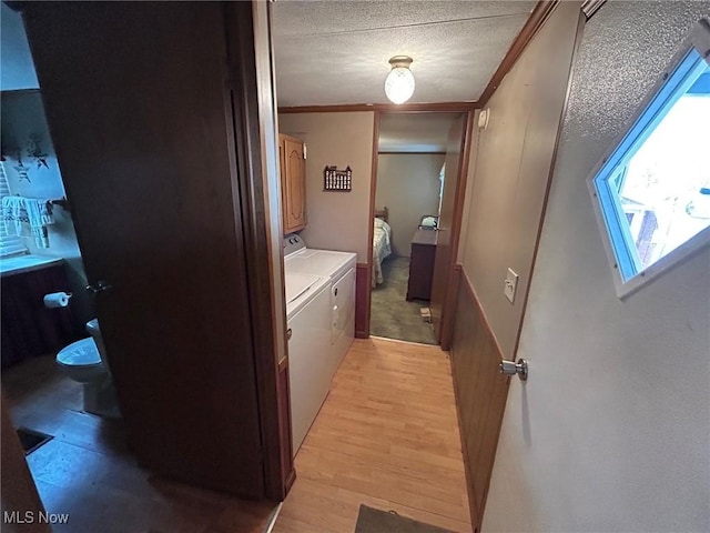 hallway featuring washing machine and dryer, a textured ceiling, light wood-style flooring, and ornamental molding