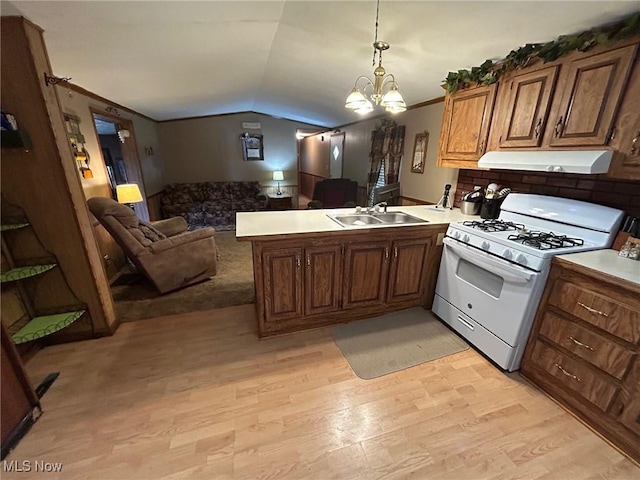 kitchen with under cabinet range hood, open floor plan, white gas range, a peninsula, and a sink