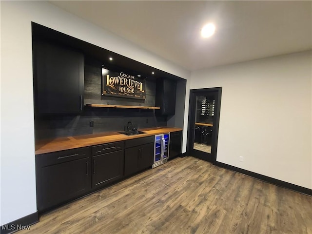 bar featuring beverage cooler, a sink, wood finished floors, wet bar, and baseboards