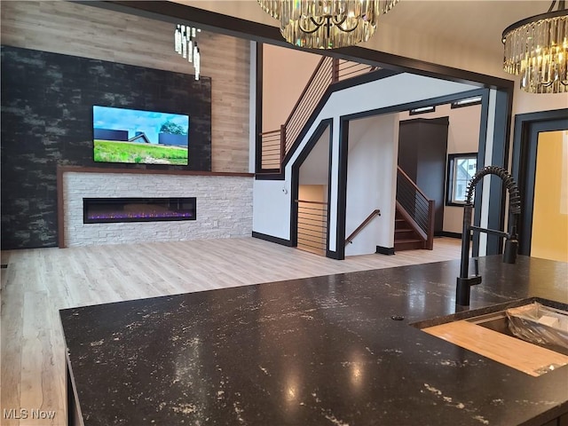 unfurnished living room with a notable chandelier, a sink, a glass covered fireplace, wood finished floors, and stairs