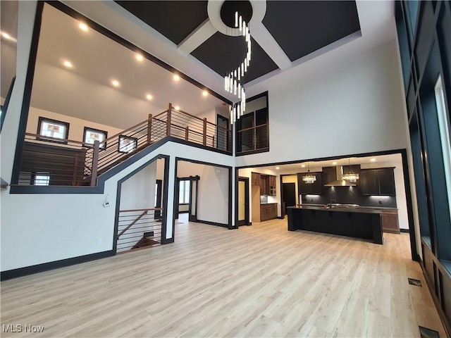 living area with visible vents, baseboards, light wood-style floors, and a towering ceiling