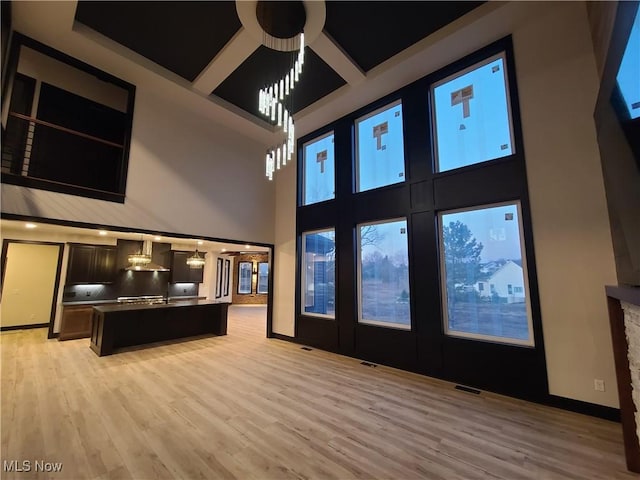 interior space with visible vents, light wood-type flooring, a high ceiling, and baseboards