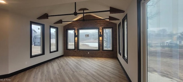 spare room with a ceiling fan, lofted ceiling with beams, wood finished floors, and baseboards