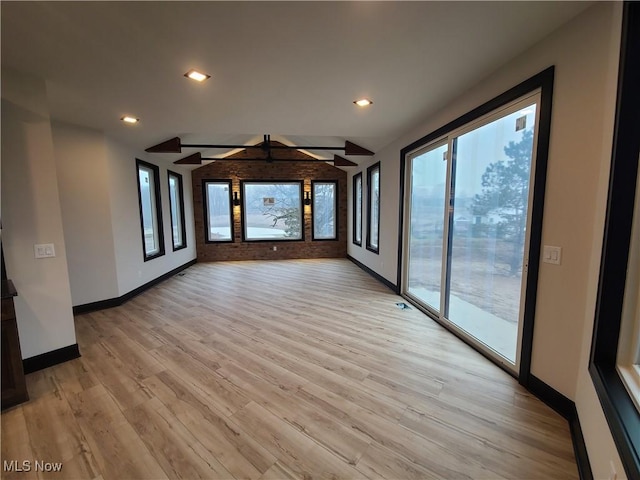 unfurnished living room with a wealth of natural light, light wood-type flooring, baseboards, and vaulted ceiling