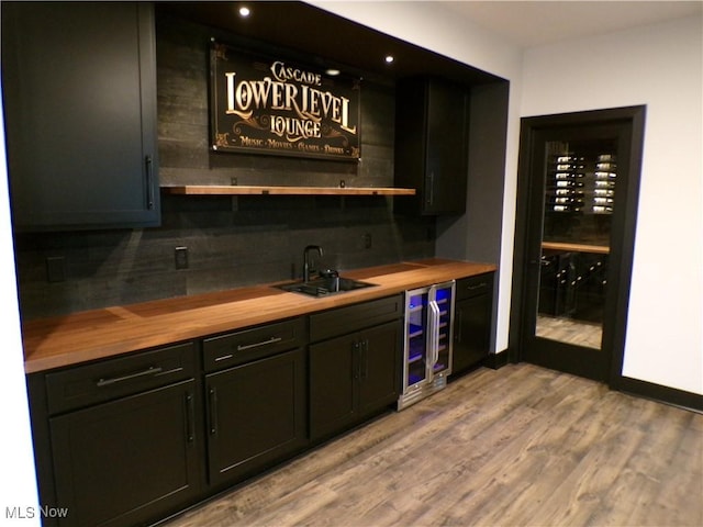 bar with backsplash, wine cooler, light wood-type flooring, wet bar, and a sink