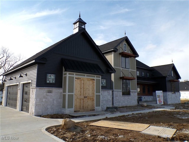 view of front facade with roof with shingles, an attached garage, a chimney, stone siding, and board and batten siding