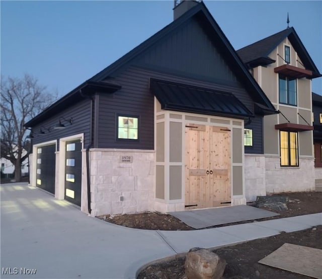 view of front of house with a garage, a standing seam roof, stone siding, metal roof, and a chimney