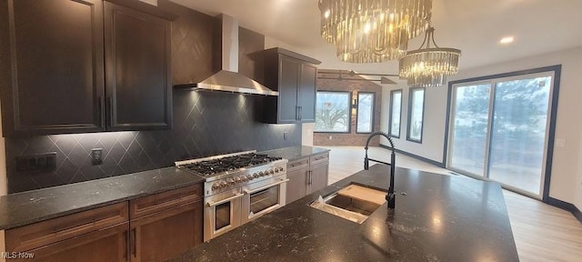 kitchen with double oven range, a sink, wall chimney exhaust hood, tasteful backsplash, and a chandelier