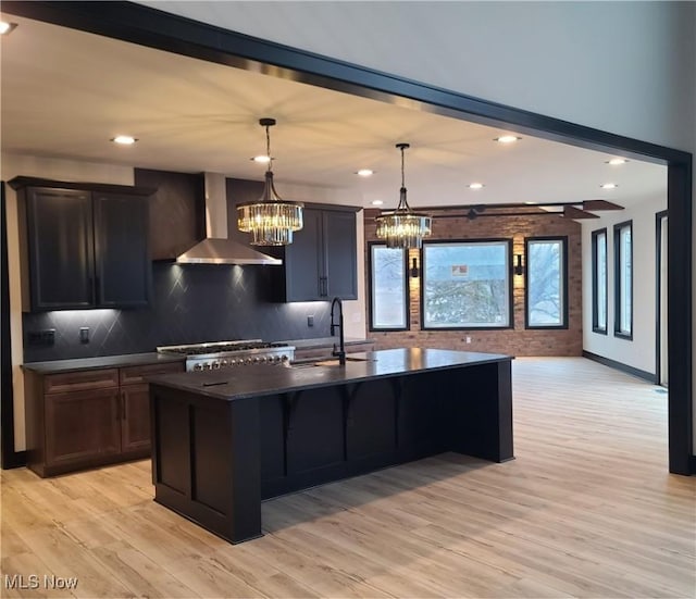 kitchen with dark countertops, tasteful backsplash, light wood-style flooring, wall chimney exhaust hood, and a sink