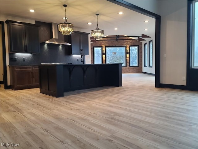 kitchen featuring dark countertops, wall chimney range hood, light wood-style flooring, and backsplash