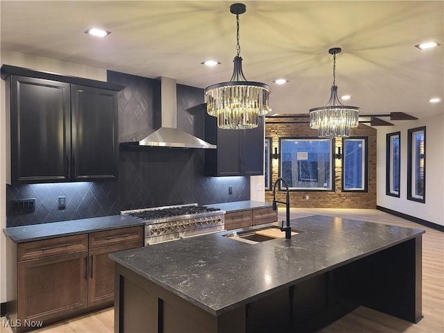 kitchen featuring tasteful backsplash, wall chimney range hood, a center island with sink, range with two ovens, and a sink