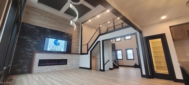 unfurnished living room with a stone fireplace, stairs, a towering ceiling, and wood finished floors