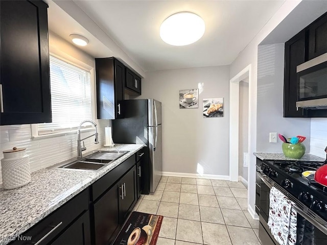 kitchen featuring light tile patterned floors, a sink, decorative backsplash, stainless steel appliances, and dark cabinets