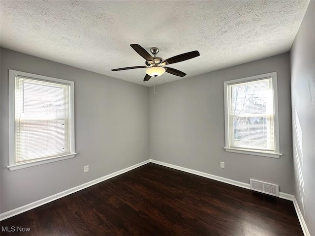 empty room with visible vents, a textured ceiling, dark wood finished floors, baseboards, and ceiling fan