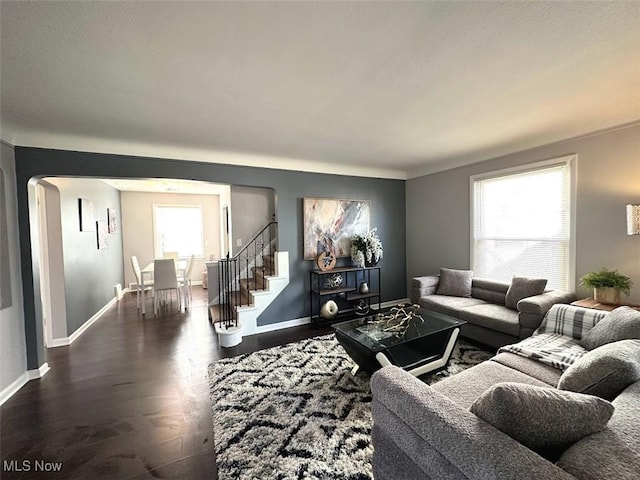 living area with arched walkways, stairway, dark wood-type flooring, and baseboards