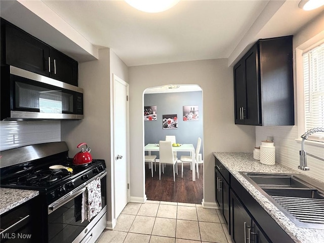 kitchen with a sink, arched walkways, appliances with stainless steel finishes, and dark cabinetry