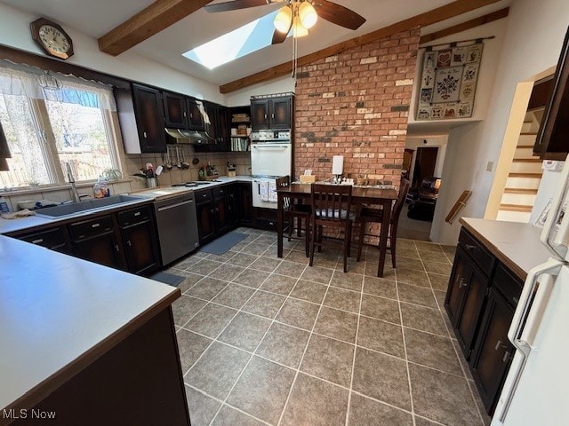 kitchen with white appliances, vaulted ceiling with skylight, light tile patterned flooring, a sink, and backsplash