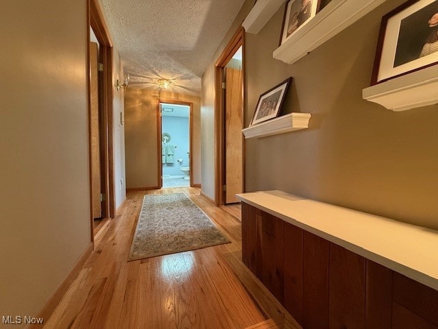 hallway with light wood-style floors, baseboards, and a textured ceiling