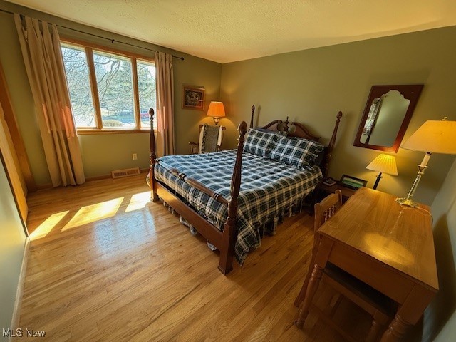 bedroom featuring light wood-style floors, visible vents, and a textured ceiling