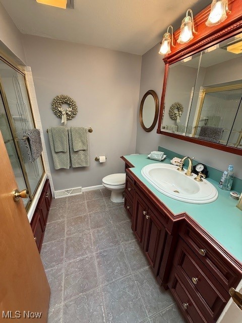 bathroom with visible vents, baseboards, toilet, combined bath / shower with glass door, and vanity