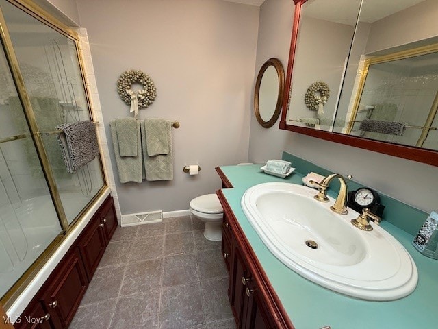 full bath featuring visible vents, baseboards, toilet, shower / bath combination with glass door, and vanity